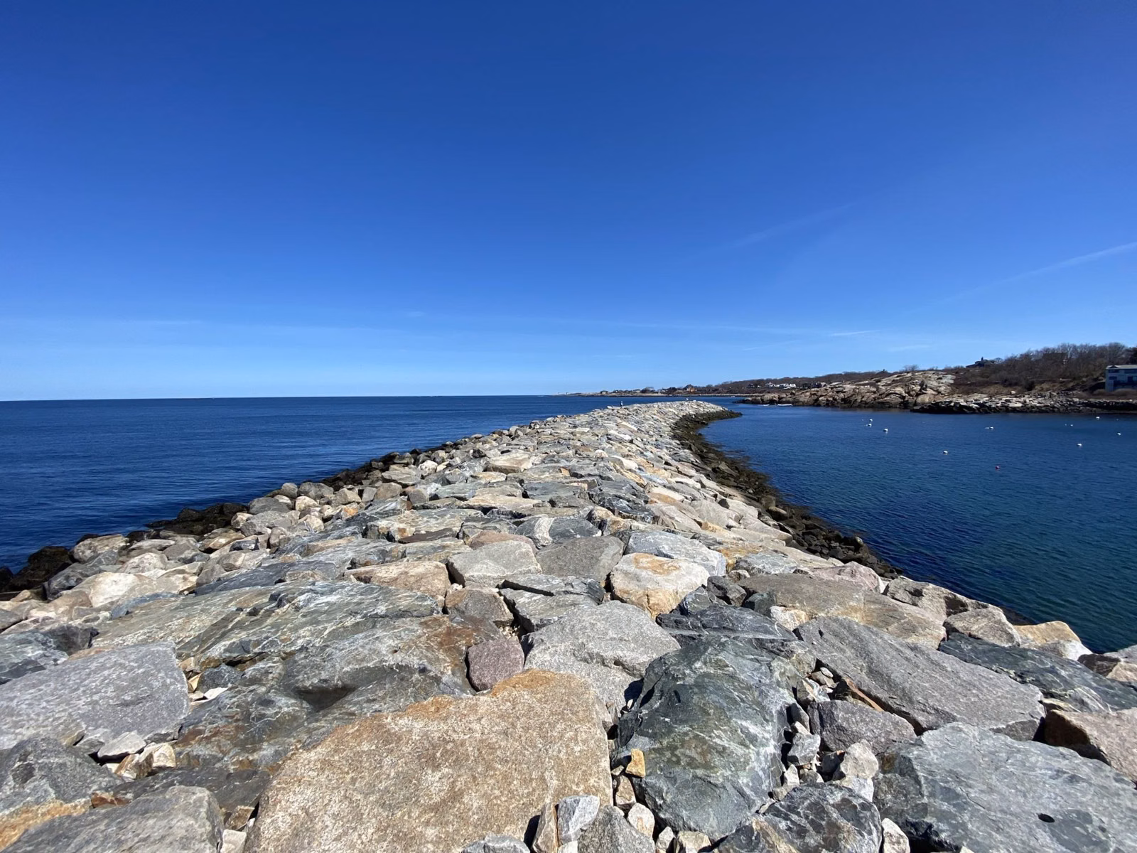 A granite-block jetty running out from Bearskin Neck between the open ocean and Rockport Harbor